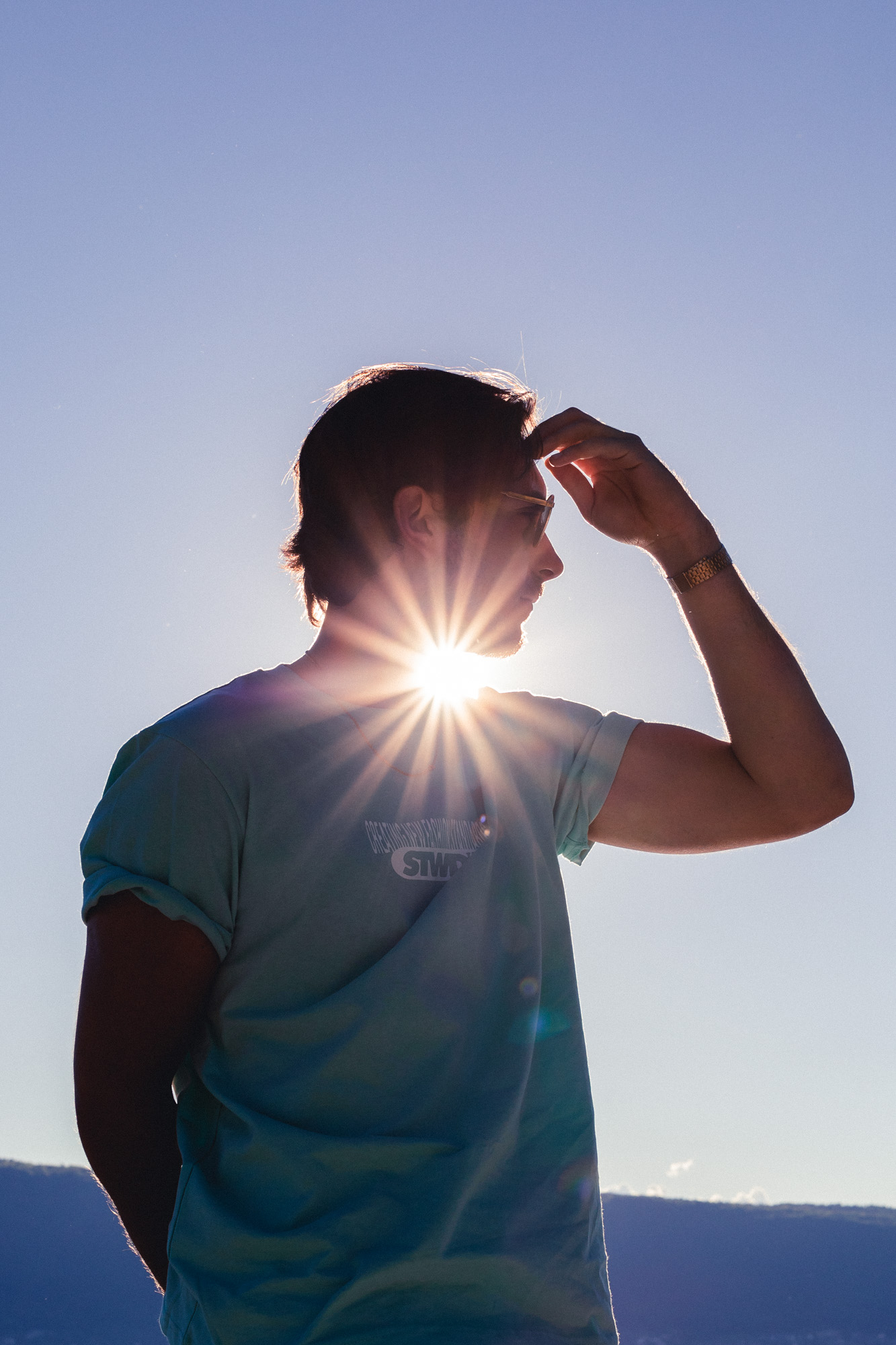photo d'un homme brun de profile, avec un t-shirt bleu, devant la lumière de soleil