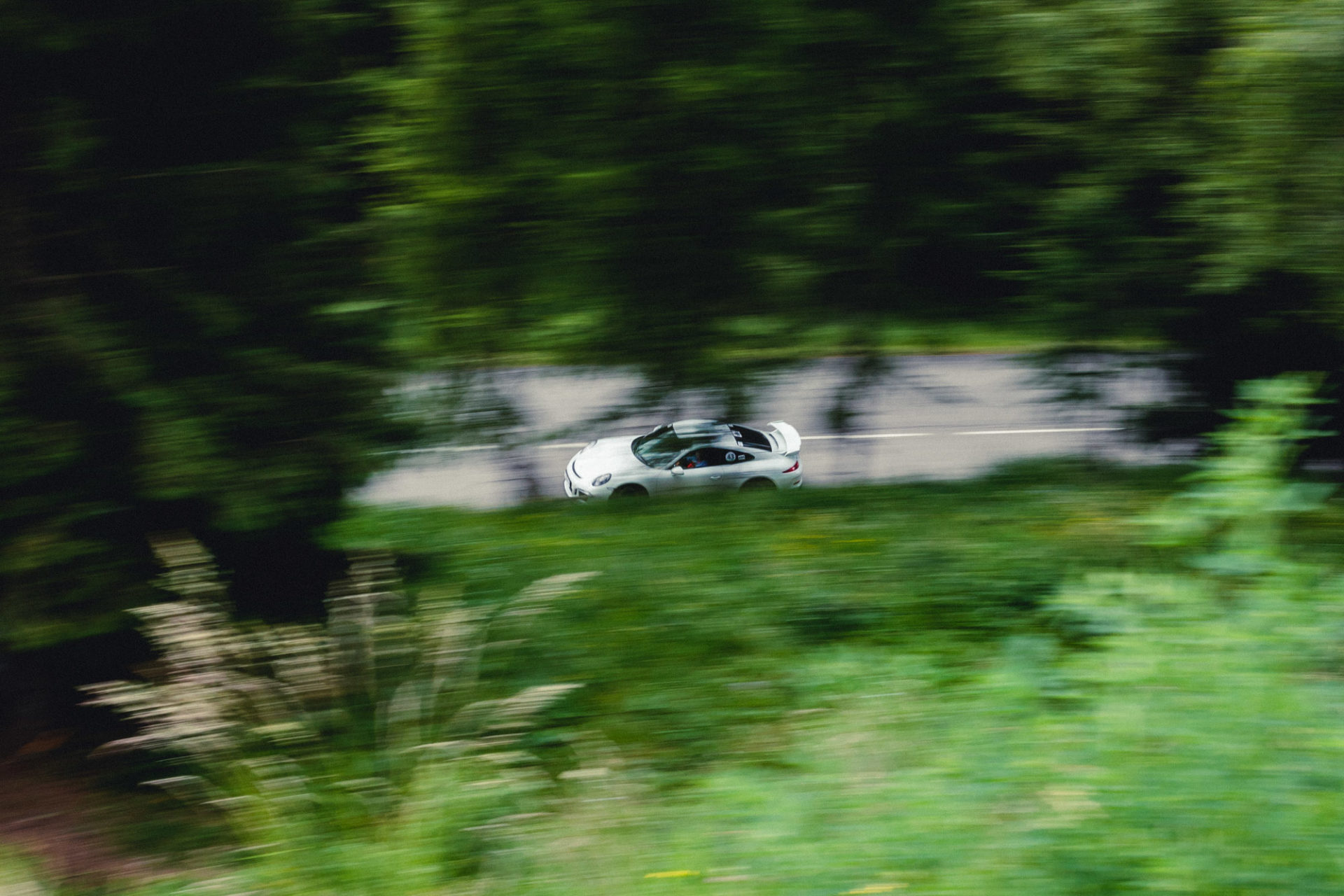 photo d'une voiture sportive blanche en mouvement entre des sapins verts