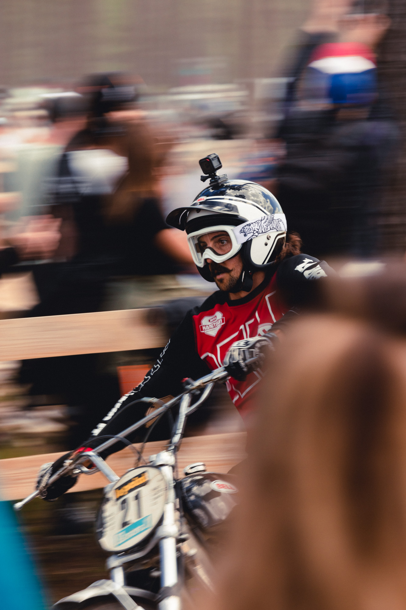 photo d'un motard à moustache sur sa moto en mouvement, casque et lunette de moto transparentes