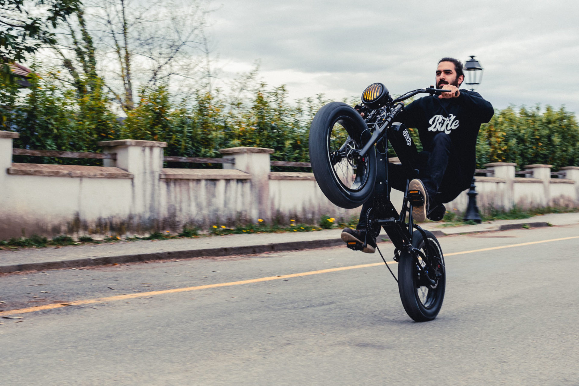 photo d'une personne faisant une roue arrière avec un vélo électrique noir ressemblant à une vieille moto