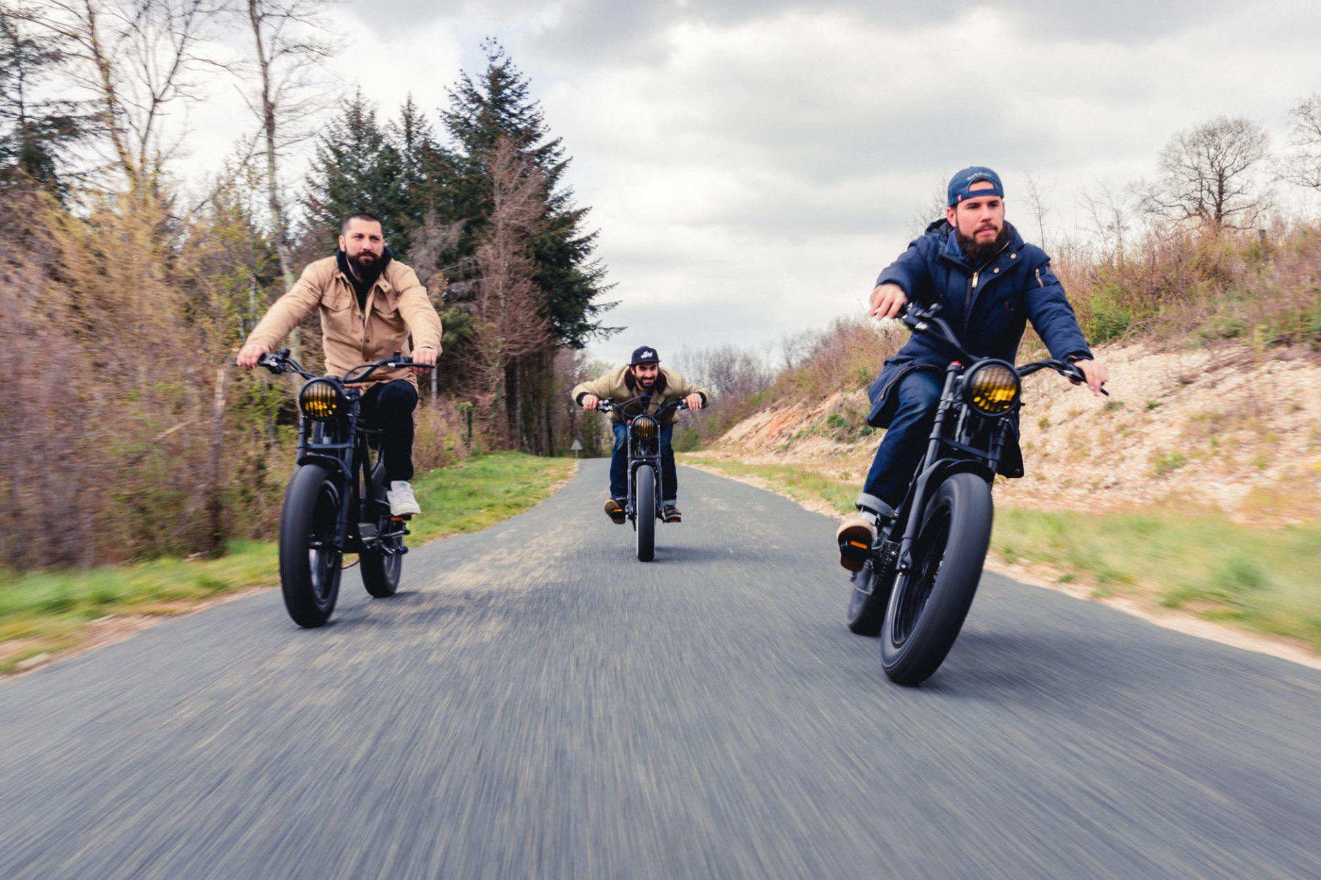 photo de trois personnes sur des vélos électrique noirs ressemblants à des vieilles motos, roulant face à la caméra sur la route