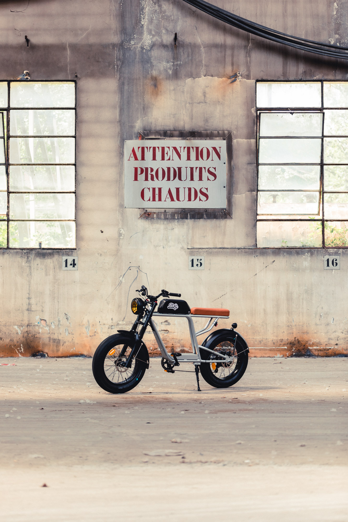 photo d'un vélo électrique gris ressemblant à une vieille moto devant un panneau avec une inscription disant attention produits chauds