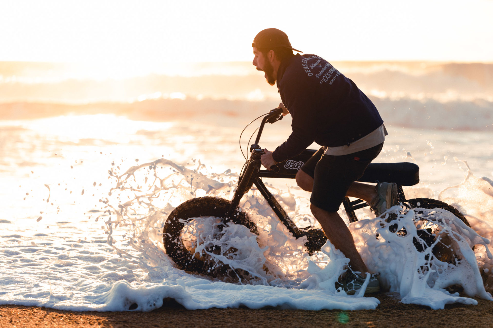 photo d'une personne criant en tenant un vélo électrique ressemblant à une vieille moto, dans une vague d'eau