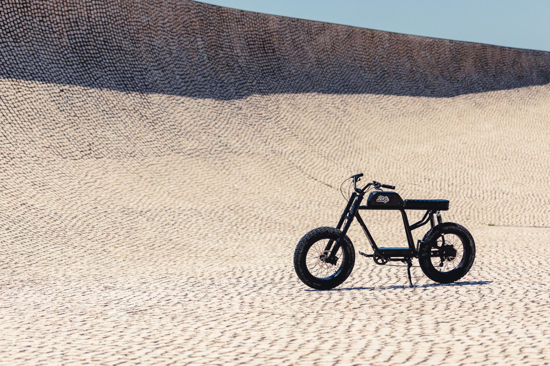 photo d'un vélo électrique noir ressemblant à une vieille moto, dans un skate-park recouvert de pavés