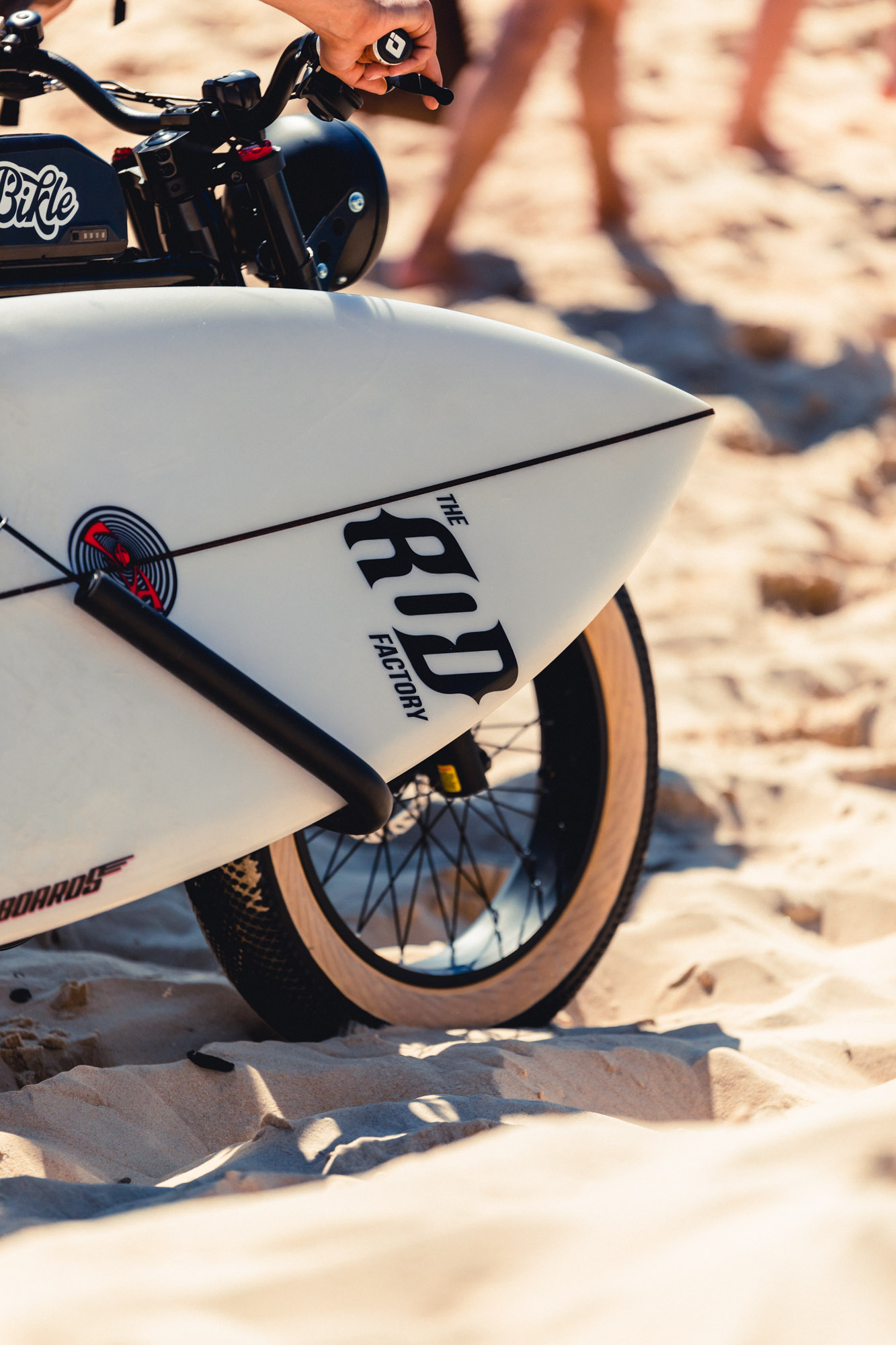 photo gros plan d'un vélo électrique noir ressemblant à une vieille moto avec un surf sur le sable