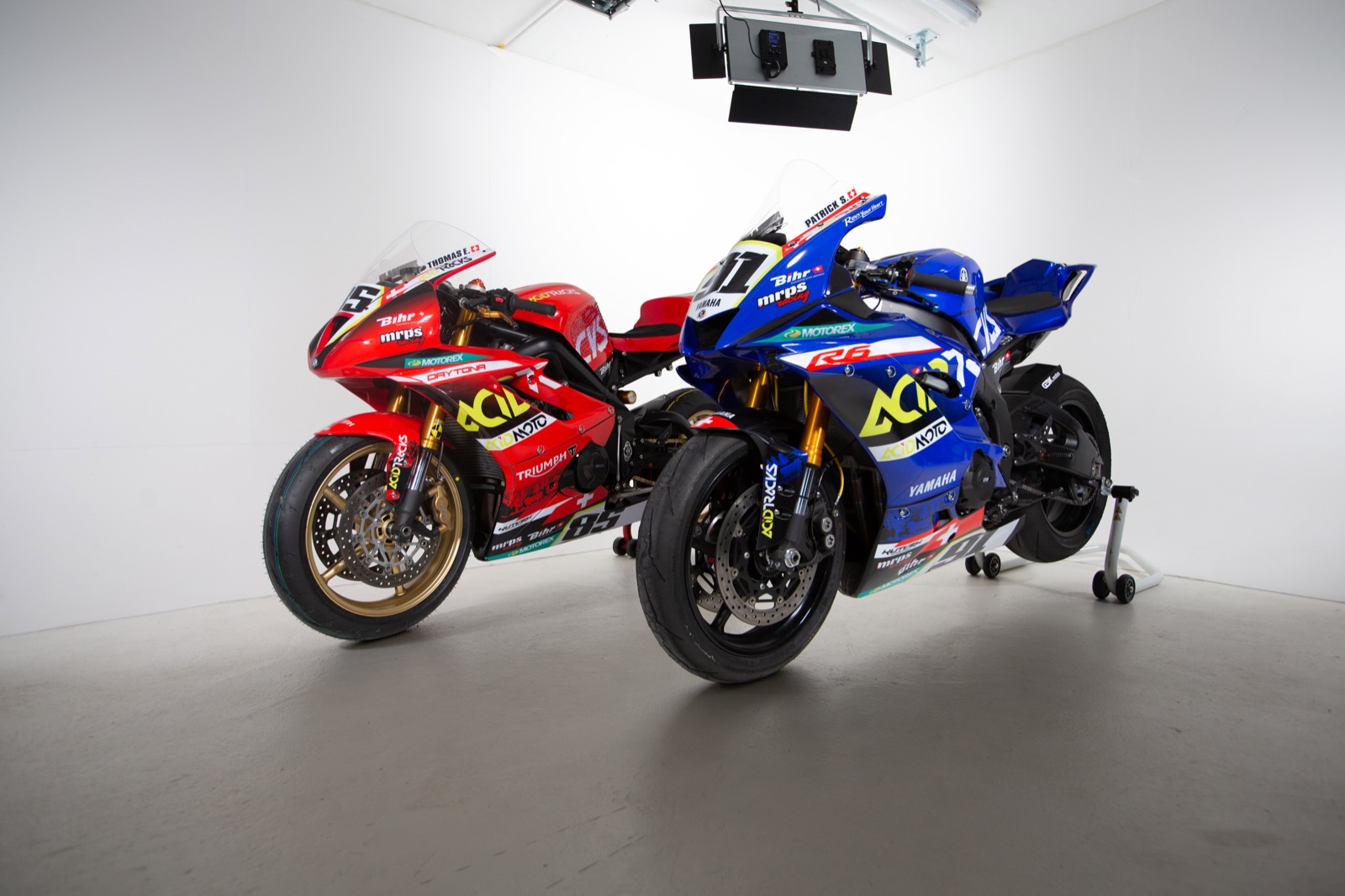 Photo de deux motos bleue de trois quart face, et rouge, floquée AcidMoto et Acidtracks, en studio fond blanc.